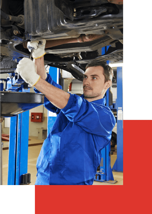 A full shot of an auto mechanic in a blue suit working on a car suspension.